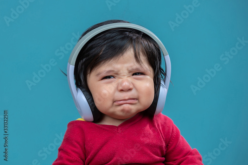 Leinwand Poster portrait of baby crying with headphones on blue background