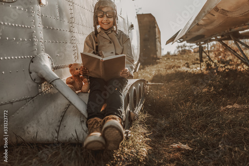 Smiling little kid reading book near plane