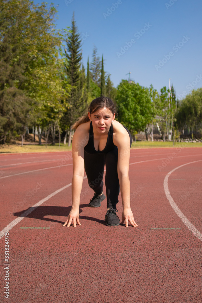 Mujer Fitness con ropa negra en pista de tartán preparándose para correr Mujer Fitness con ropa negra en pista de tartán preparándose para correr