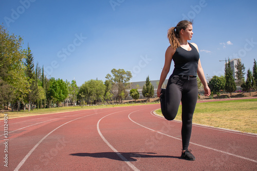 Mujer Fitness con ropa negra en pista de tartán realizando ejercicios de calentamiento durante un día soleado photo