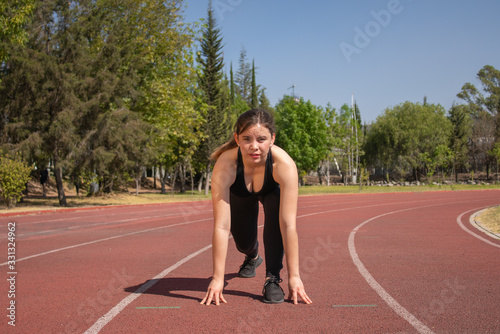 Mujer Fitness con ropa negra en pista de tartán preparándose para correr 