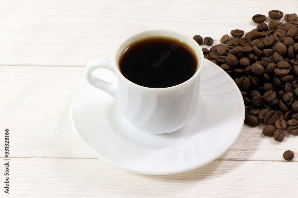 Fototapeta premium A white cup of coffee and coffee beans on a wooden table.