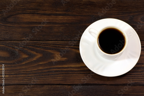 A white cup of coffee and coffee beans on a wooden table.