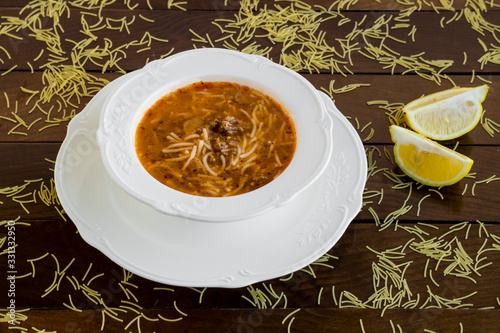 Traditional Turkish vermicelli soup,in the stylish soup set on the wooden table with slices of lemon. photo