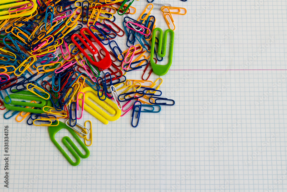 Fototapeta premium Colorful paperclips heap on the white,checkered paper surface with copy space.Conceptual image of education.