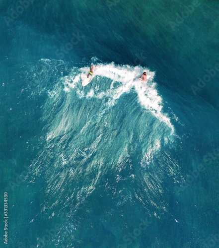 Two surfers in the ocean catch a wave. shot from above