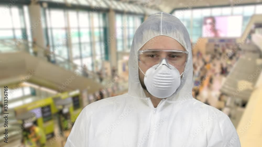 Man in white respiratory mask and clothing looking around. Fear and panic. Crowded indoors background in a mall market or airport.