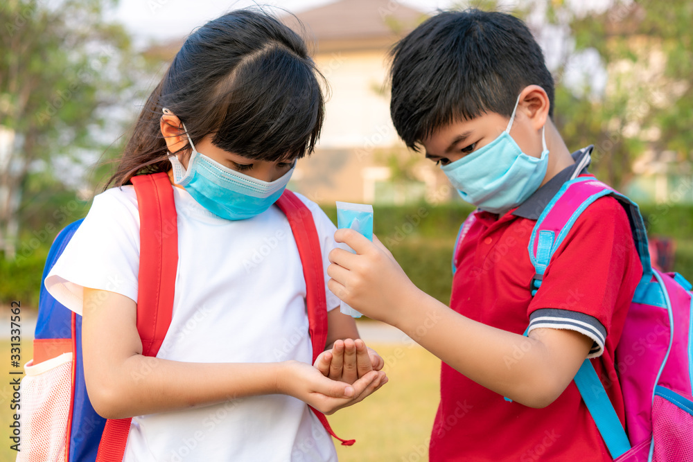 Asian boy student wear hygienic mask and press alcohol gel from bottle to hand's sister for protect  covid-19 coronavirus and epidemic virus after back from school..