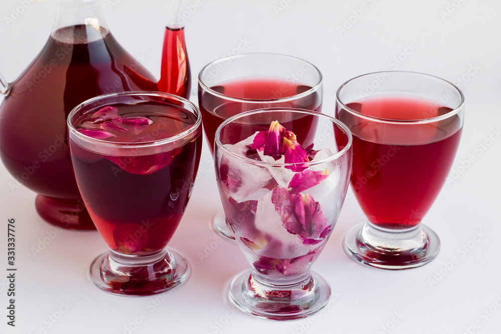 Sweet,cold red rose sherbet in glass and pitcher with red rose ice cubes on white.Traditional drinks of Ramadan. Sweet,cold red rose sherbet in glass and pitcher with red rose ice cubes on white.Traditional drinks of Ramadan.