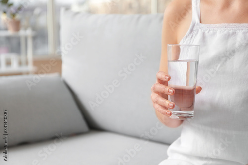 Beautiful young woman with glass of water at home, closeup