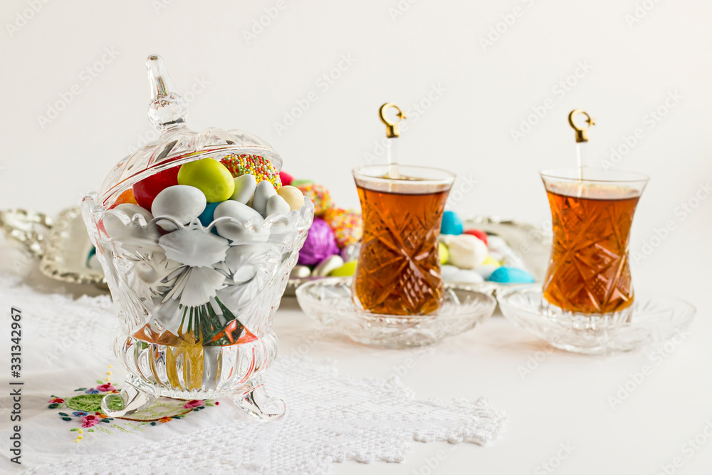 Colorful almond candies in the stylish,crystal candy bowl on the white table with Turkish Tea.The Sugar Feast end of Ramadan.