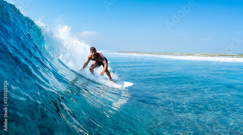Young man surfs ocean wave in Maldives