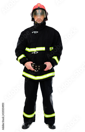 Full-length portrait of a man in black uniform of a fireman with a red helmet on a white isolated background. The model stands right in front of the camera. Studio photo.