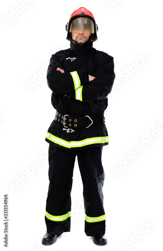 Full-length portrait of a man crossed his arms over his chest in a black uniform of a fireman with a red helmet on a white isolated background. The model stands right in front of the camera. © Вячеслав Чичаев