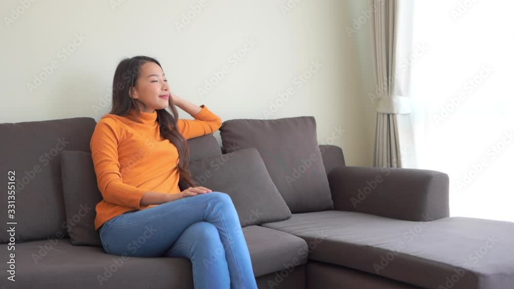Beautiful Asian woman wearing orange sweater sitting on couch looking outside Beautiful Asian woman wearing orange sweater sitting on couch looking outside
