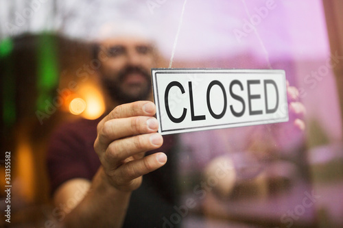 small business, people and crisis concept - owner puts closed sign at bar or restaurant glass door or window photo