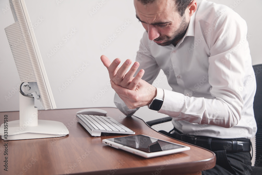 Caucasian businessman suffering from hand pain in office. Caucasian businessman suffering from hand pain in office.