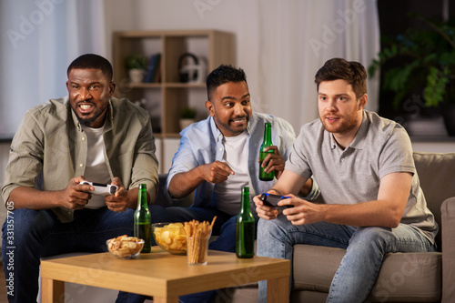 friendship  technology and leisure concept - smiling male friends with gamepads and beer playing video game at home at night