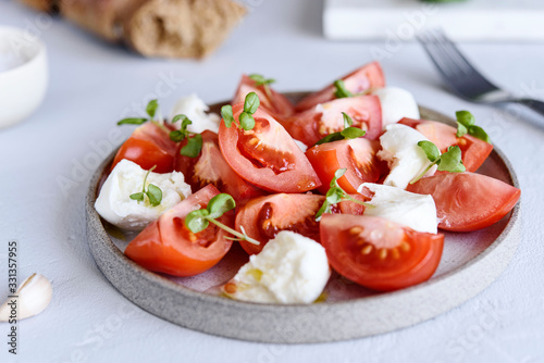 Italian Сaprese salad with sliced tomatoes, mozzarella cheese, basil, olive oil in a plate on grey concrete table. Selective focus