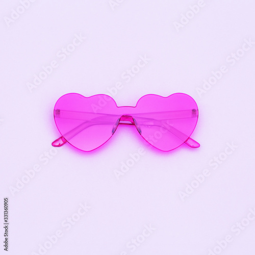 Minimal style fashion photography with heart shaped glasses on purple background with copy space. Pink modern sunglasses and reflection of palm leaf. Trendly summer concept.