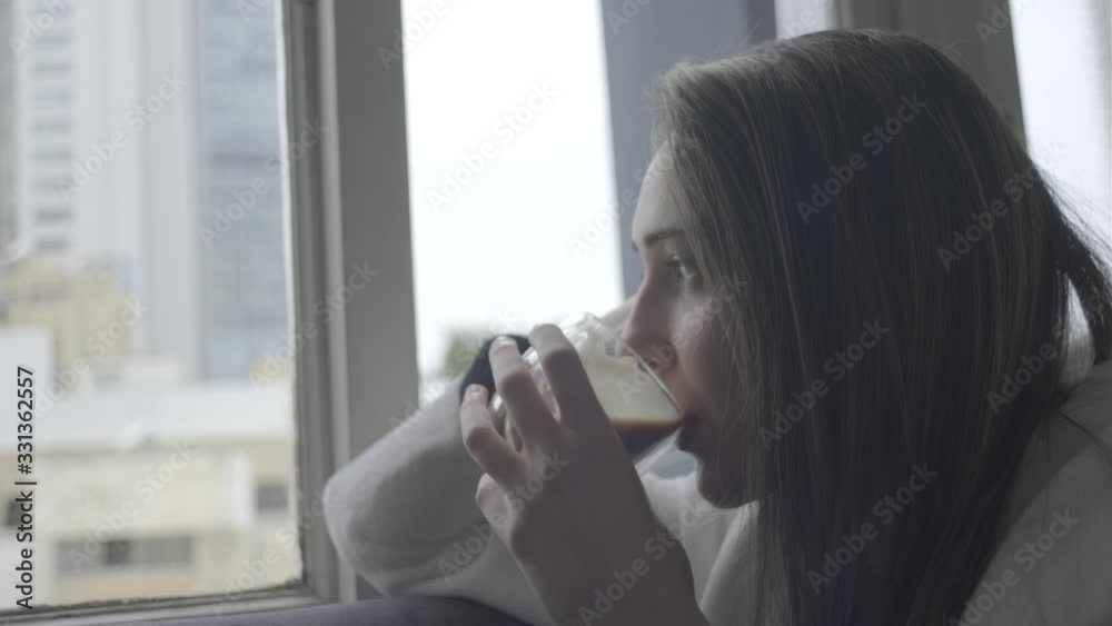beautiful young woman looking through the window drinking coffee beautiful young woman looking through the window drinking coffee