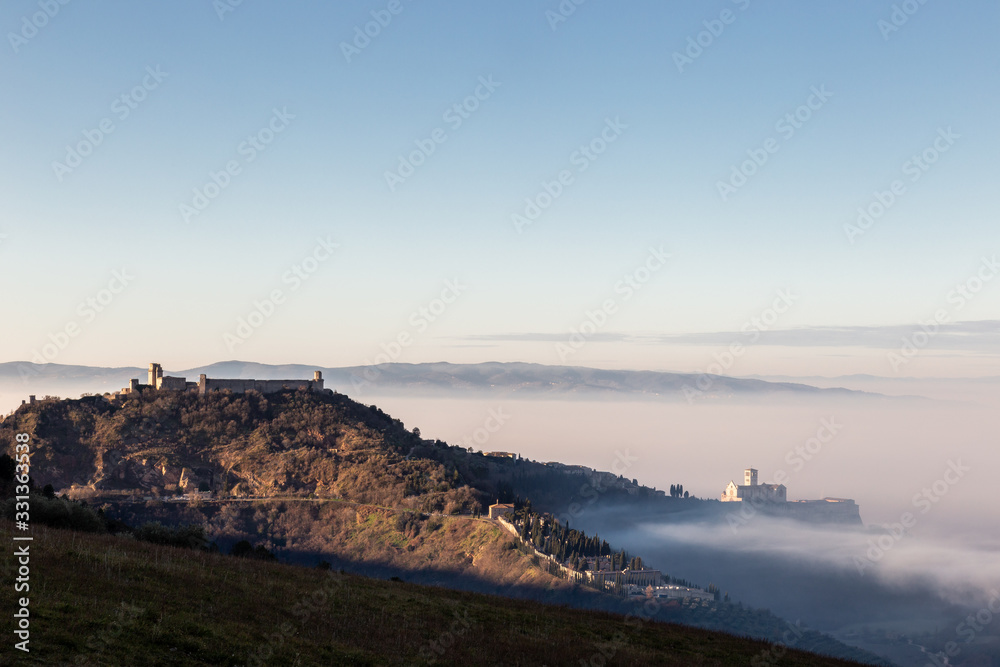 An epic view of St.Francis church in Assisi town (Umbria) above a sea of fog at dawn