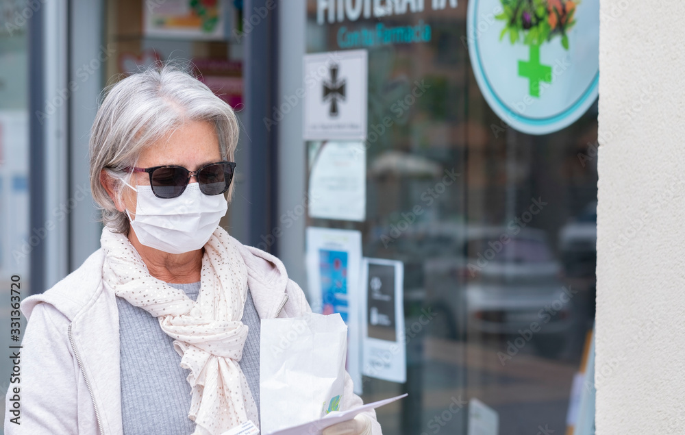 Senior lady with mask and protective gloves leaves the pharmacy with medicines and instructions. Fear of coronavirus infection, covid-19. Concept of retired senior and fear of contagion