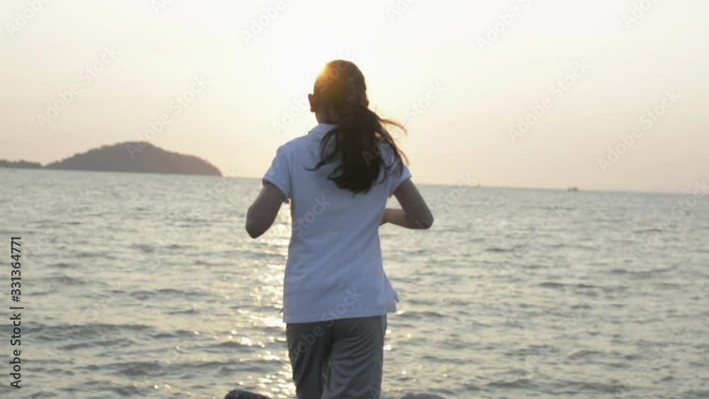 Rear view of asian little girl jogging to the coast and raises arms into air during sunrise in phuket. Thailand. Slow motion. Rear view of asian little girl jogging to the coast and raises arms into air during sunrise in phuket. Thailand. Slow motion.