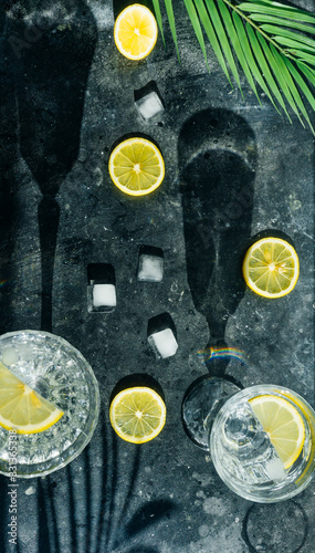 Water lemon detox. Pure cold water with lemon in crystal glasses on a dark background in the sunny summer sun