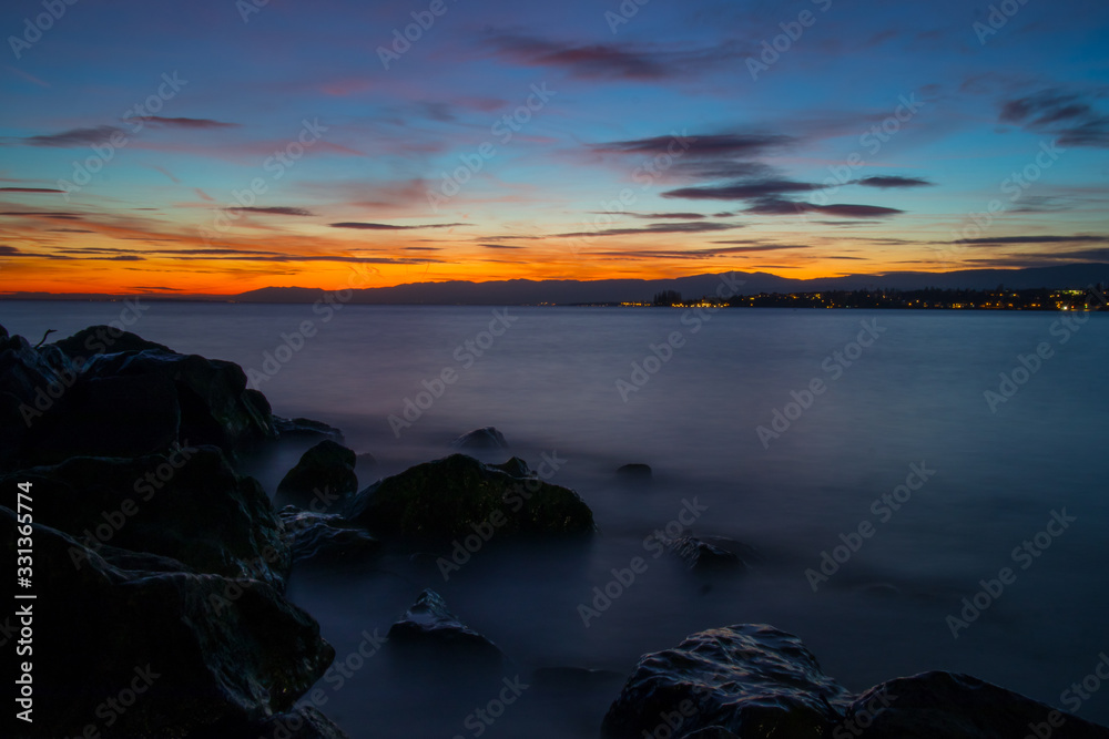 Beautiful evening photo of Lac Leman close to Lausanne, with sun just behind the horizon and long exposure of water. Beautiful evening photo of Lac Leman close to Lausanne, with sun just behind the horizon and long exposure of water.