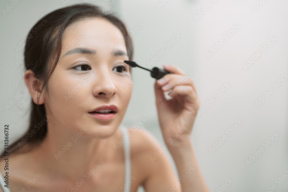 Young woman dyes her eyelashes with mascara brush. Young beautiful woman applying mascara makeup on eyes at bathroom.