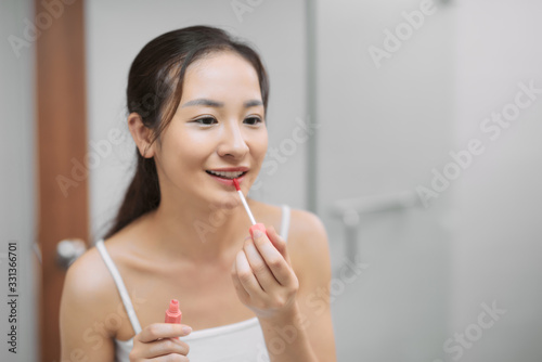 Young woman applying gloss for lips looking at mirror