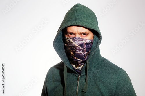 A man wearing a mask and a hood looks into the camera. Close up