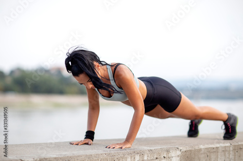Athletic woman with perfect body shape exercise pushups outdoor