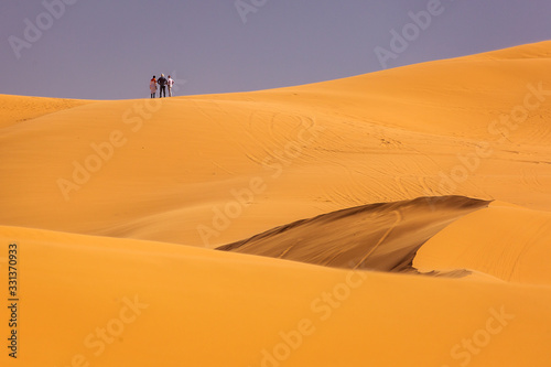 Three people on top of dunes in Desert Sahara with beautiful lines and colors at sunrise. Merzouga  Morocco