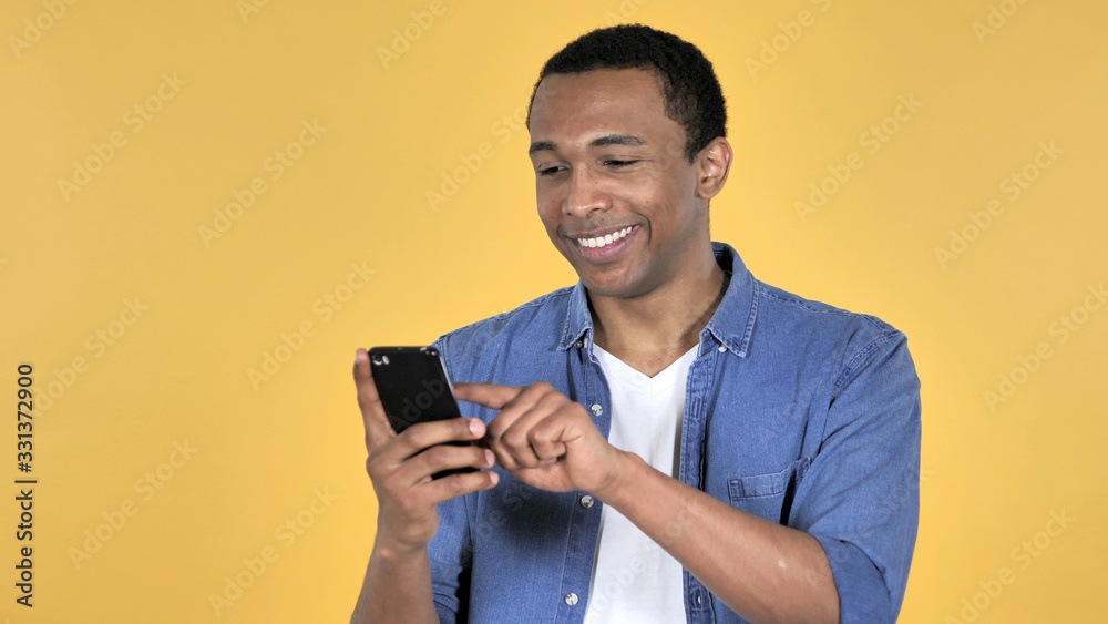 Young African Man Browsing Smartphone Isolated on Yellow Background Young African Man Browsing Smartphone Isolated on Yellow Background