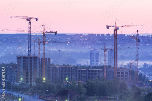 Tower cranes, the construction of a new tall apartment building at a construction site in the city at sunset or sunrise. Development, construction industry concept