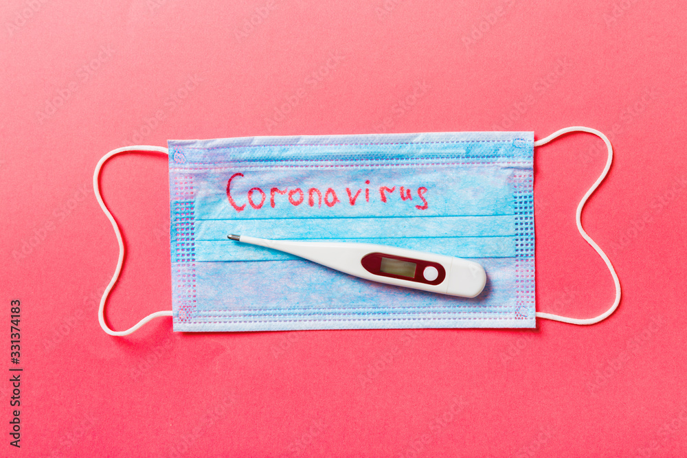 Top view of protective medical mask and a thermometer on red background. Coronavirus word. Ncov and covid epidemic. Pandemic concept. Protect your health