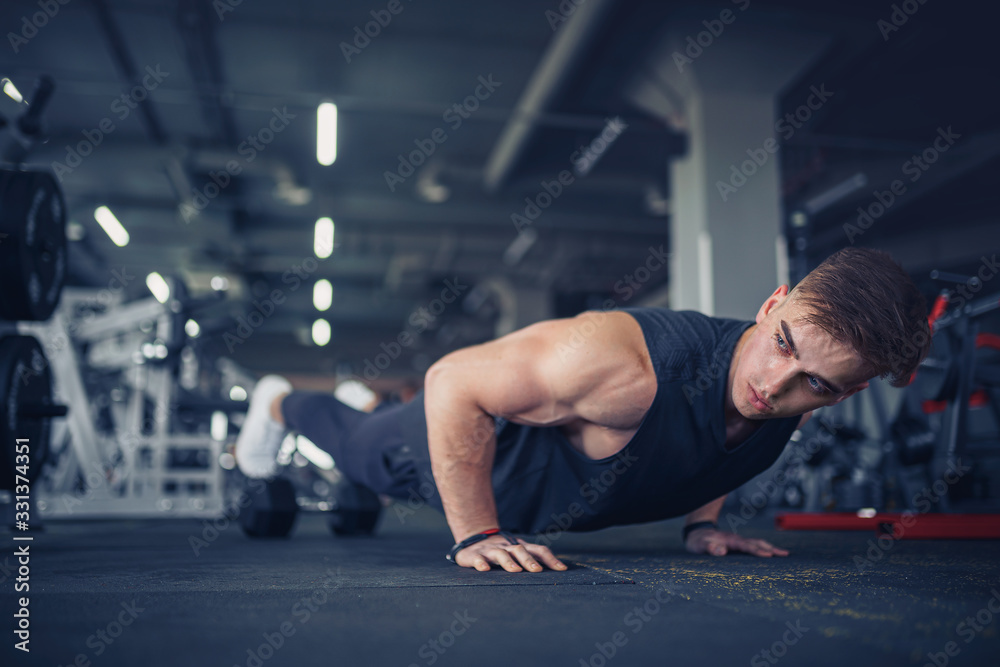 Fototapeta premium Young athletic man doing push-ups in gym. Muscular and strong guy exercising