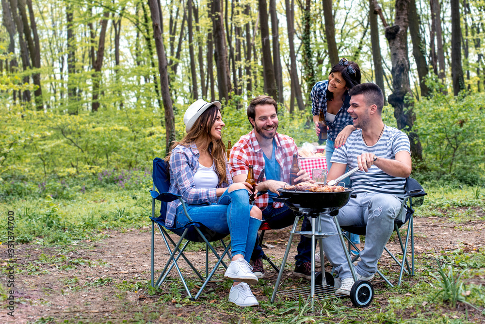Group of friends making barbecue in nature and enjoying picnic day together