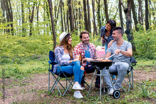 Group of friends making barbecue in nature and enjoying picnic day together