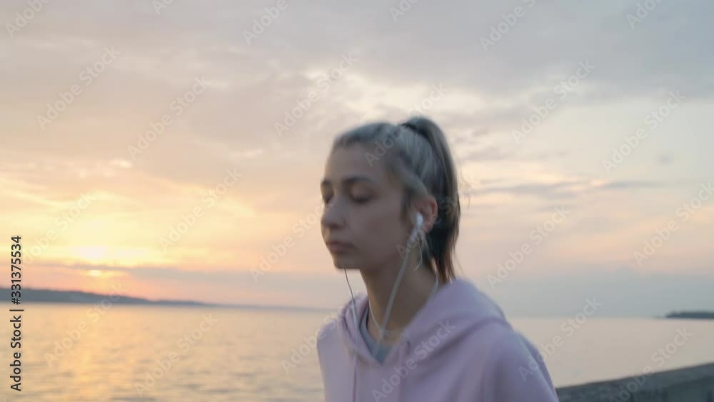 Young girl in headphones runs on a background of sunset and water, slow motion Young girl in headphones runs on a background of sunset and water, slow motion