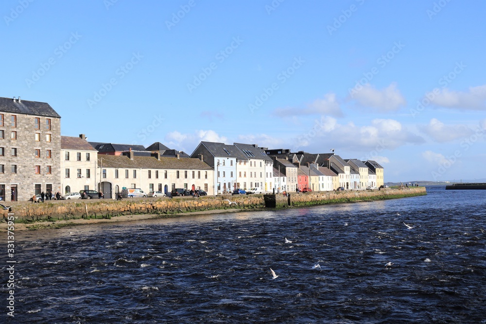 view of the Long Walk, Galway city in the distance,  blue river water in the foreground