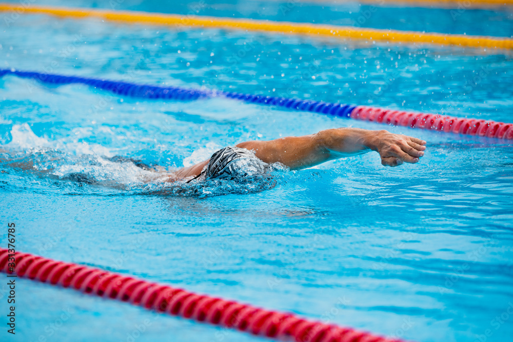Athletic man swimming in front crawl style in the swimming pool with clear blue water.