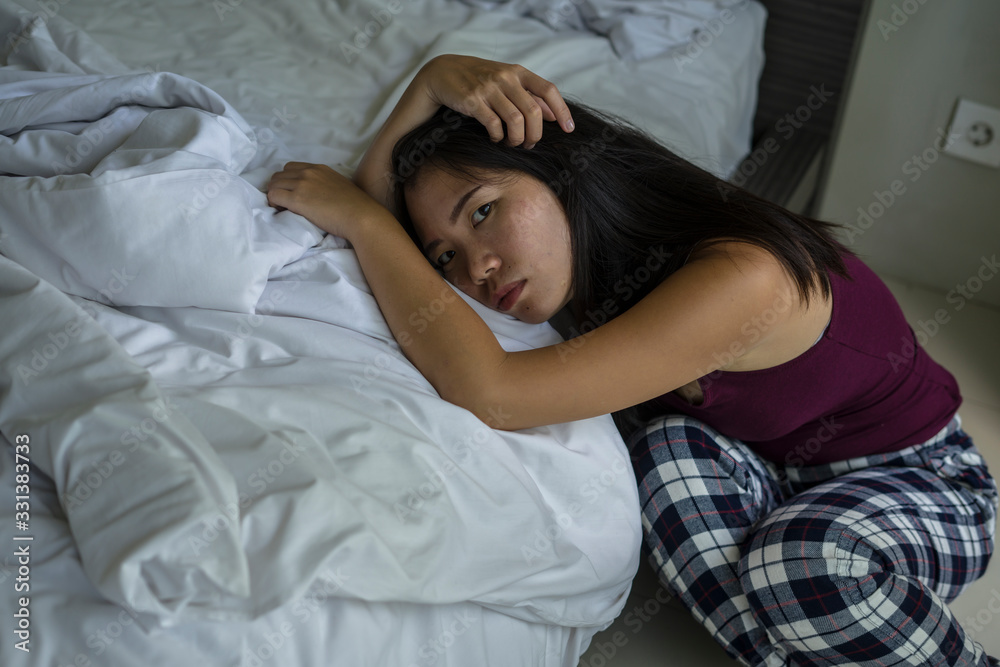 indoors portrait of young attractive sad and depressed Asian Chinese woman at home on bedroom floor leaning on bed emotional and thoughtful feeling worried and scared