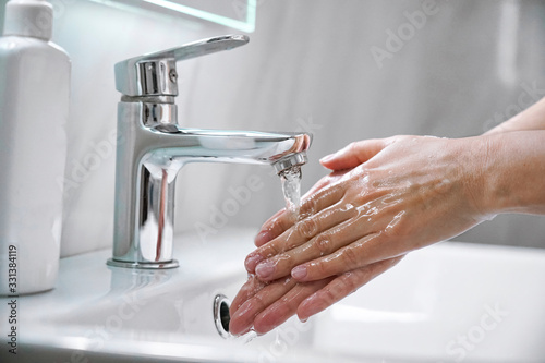 Young woman washing hands with soap over sink under faucet with water in bathroom. Girl doing cleaning hygiene routine to prevent coronavirus infection,disinfect skin care, microbe protection concept.