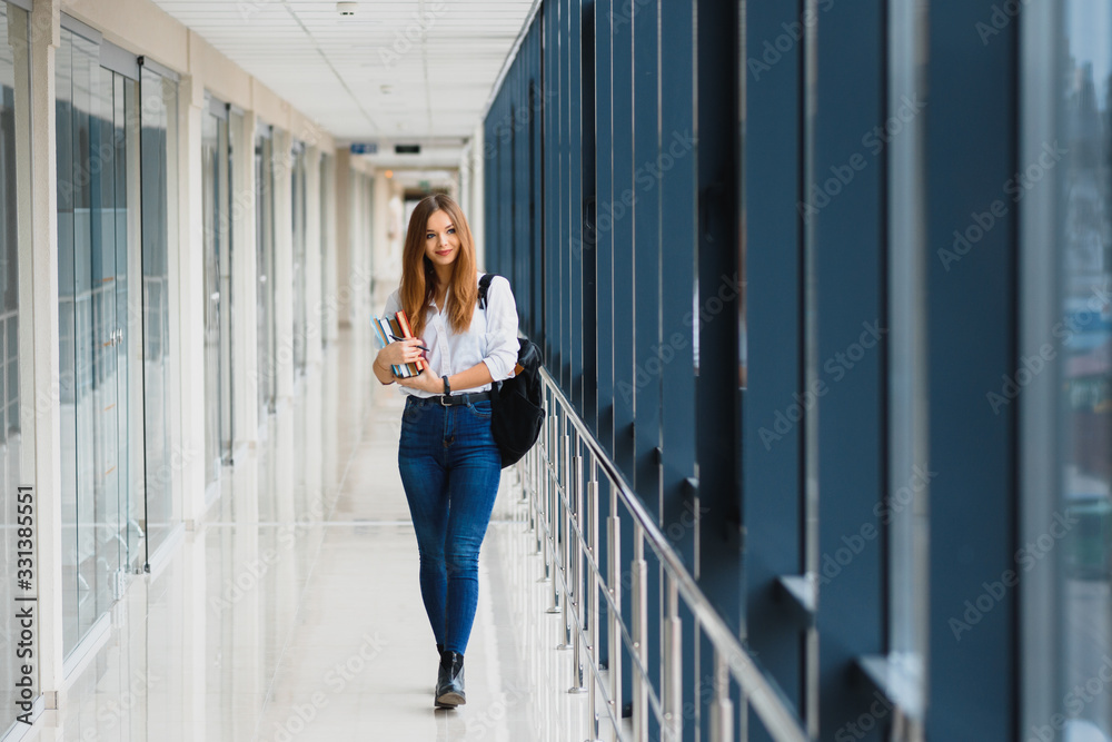 Portrait of a pretty female student with books and a backpack in the university hallway