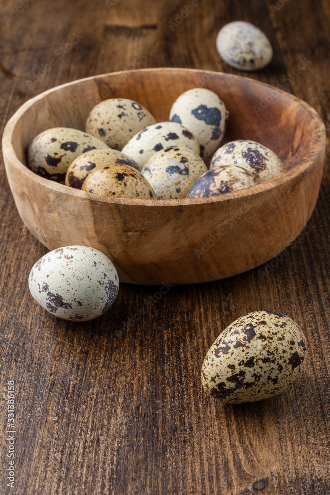Closeup of speckled quail eggs in unfocused wooden bowl and loose eggs on wooden table in portrait with copy space Closeup of speckled quail eggs in unfocused wooden bowl and loose eggs on wooden table in portrait with copy space