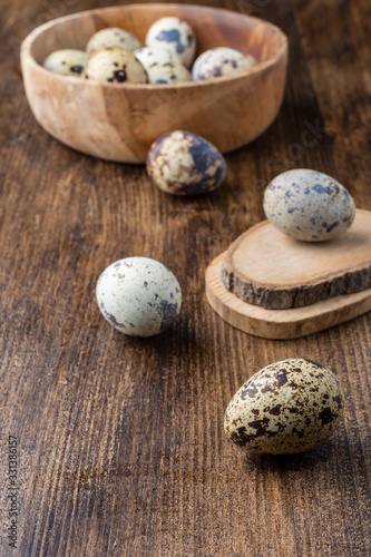 Top view of quail eggs, in the background in wooden bowl, with selective focus on dark wooden table in vertical