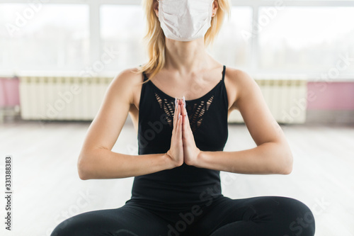 A girl in a medical mask does yoga in a closed Studio in sports clothes. Quiet meditation in the face of a virus epidemic. Close up
